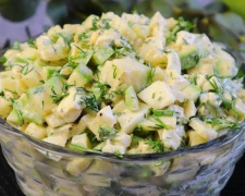 Яскравий літній салат із зеленими стрічками цукіні, кружальцями огірків, шматочками білої бринзи та свіжою зеленню, заправлений оливковою олією у білій мисці.
